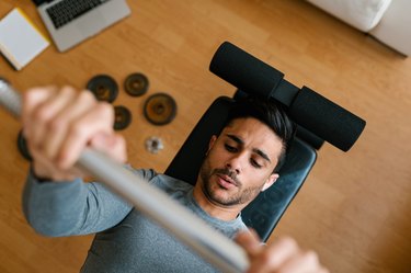 Hispanic athlete doing barbell bench press as part of a chest and shoulder workout