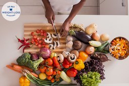 Woman on a weight-loss diet chopping a variety of vegetables in her kitchen