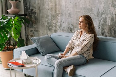 a woman sits on a blue therapist's couch near a table with a box of tissues and notebook during a session to discussion ADHD and anxiety symptoms