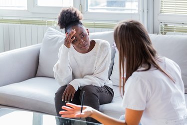 a person on a white couch talking with a mental health professional in their office