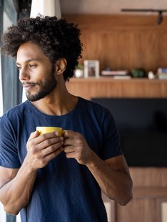 A young black man leaning up against a window with a cup of coffee 